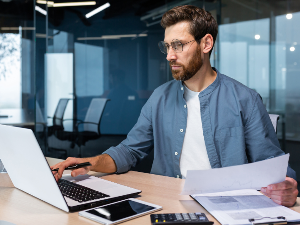 Financieel adviseur berekent EBITBA op laptop met documenten en rekenmachine in een moderne kantooromgeving.